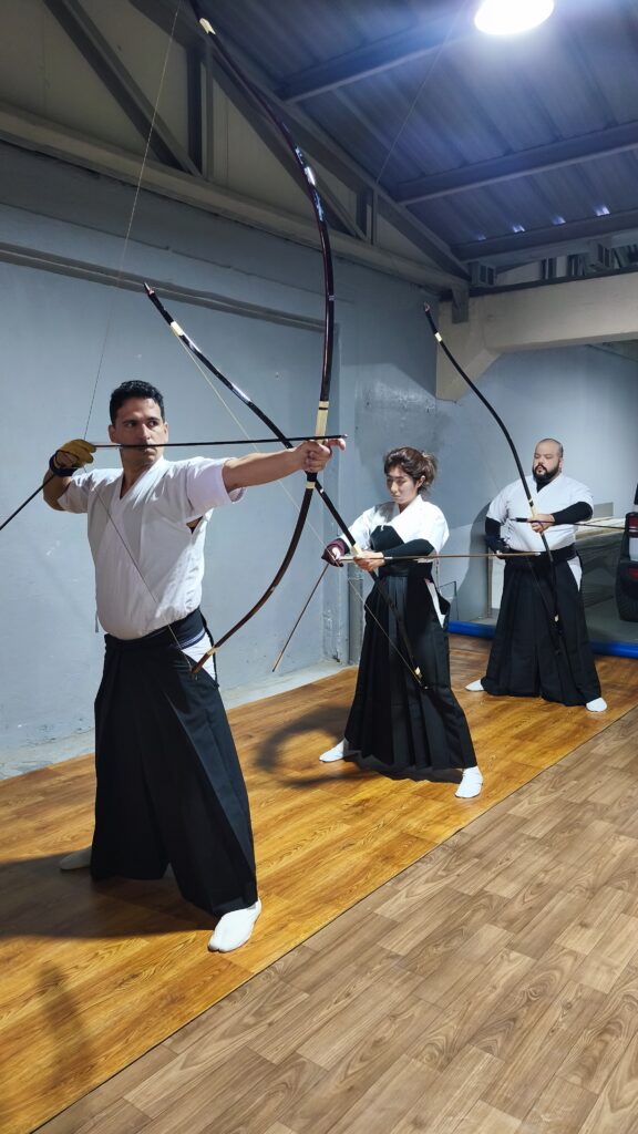 3 practicantes de kyudo disparando en un dojo